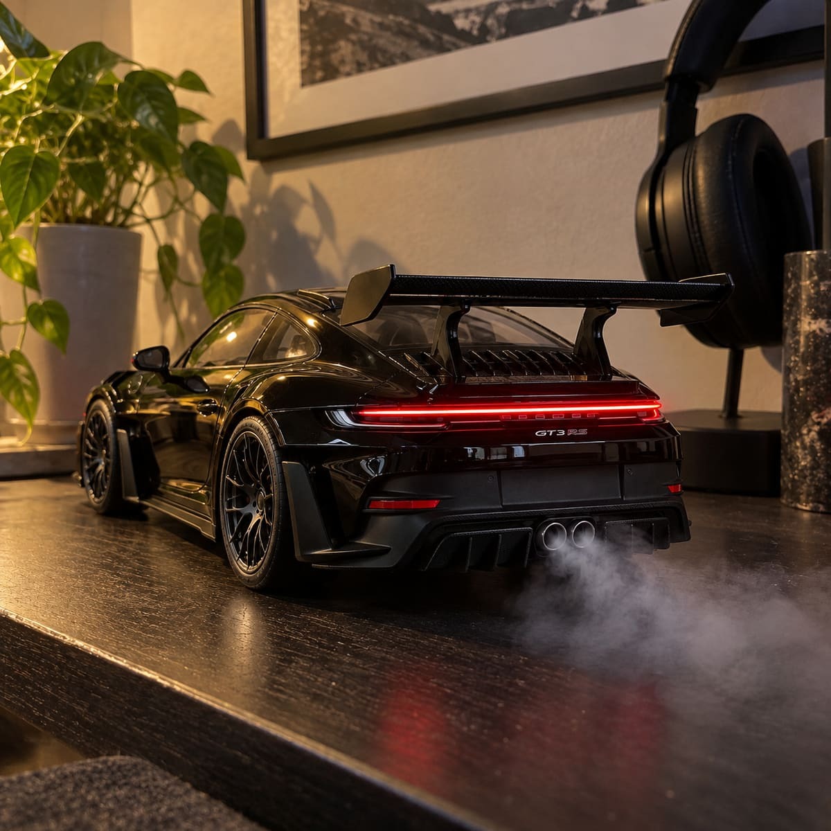 Black 911 GT3 RS model on a desk with swan-neck rear wing, full-width tail light on and smoke from twin exhausts